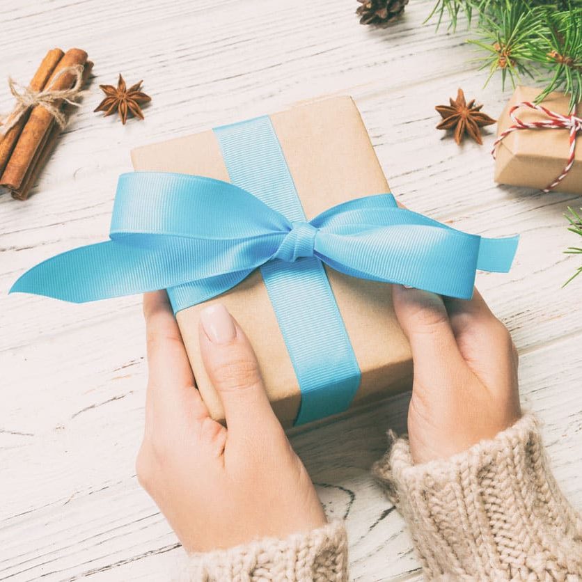 Female hands holding handmade present box in recycled paper on white wooden table background. christmas preparation concept, Gift wrapping background. Toned.