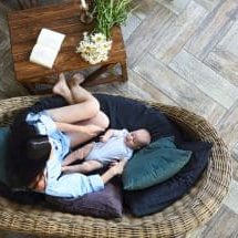 Overhead barefoot woman with cute baby relaxing on comfortable couch in cozy room at home