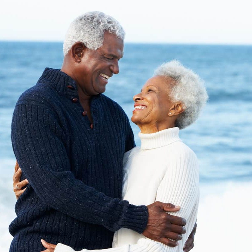 Romantic Senior Couple Hugging On Beach In Daytime Smiling At Each Other